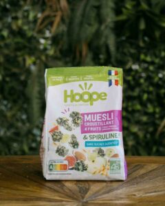 1 sachet de muesli 4 fruits posé sur une table en bois avec un fond de mur végétal