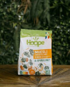 un sachet de muesli 3 noix posé sur une table en bois avec un fond de mur végétal