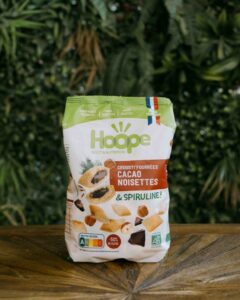 un sachet de crousti'fourrées cacao noisette posé sur une table en bois avec un fond de mur végétal