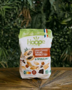 un sachet de crousti'fourrées cacao noisette posé sur une table en bois avec un fond de mur végétal