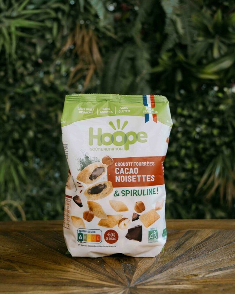 un sachet de crousti'fourrées cacao noisette posé sur une table en bois avec un fond de mur végétal