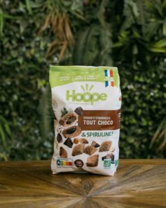 un sachet de crousti'fourrées tout choco posé sur une table en bois avec un fond de mur végétal