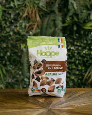 un sachet de crousti'fourrées tout choco posé sur une table en bois avec un fond de mur végétal