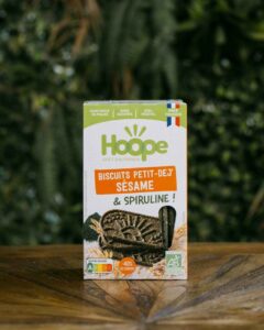 un paquet de biscuits petit déj sésame posé sur une table en bois avec un fond de mur végétal
