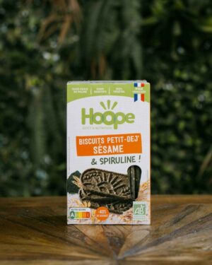 un paquet de biscuits petit déj sésame posé sur une table en bois avec un fond de mur végétal