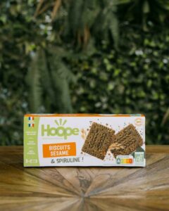 un paquet de biscuit encas sésame posé sur une table en bois avec un fond de mur végétal
