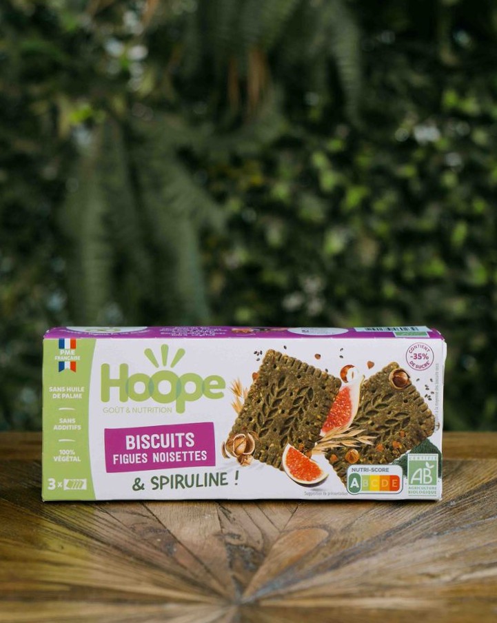 un paquet de biscuit encas figue noisette posé sur une table en bois avec un fond de mur végétal