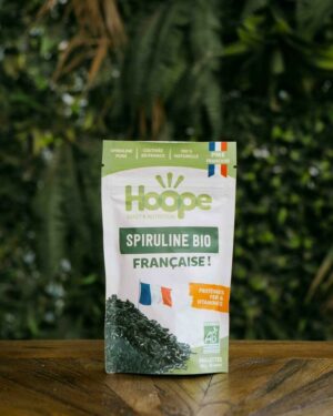un sachet de spiruline en paillette posé sur une table en bois avec un fond de mur végétal
