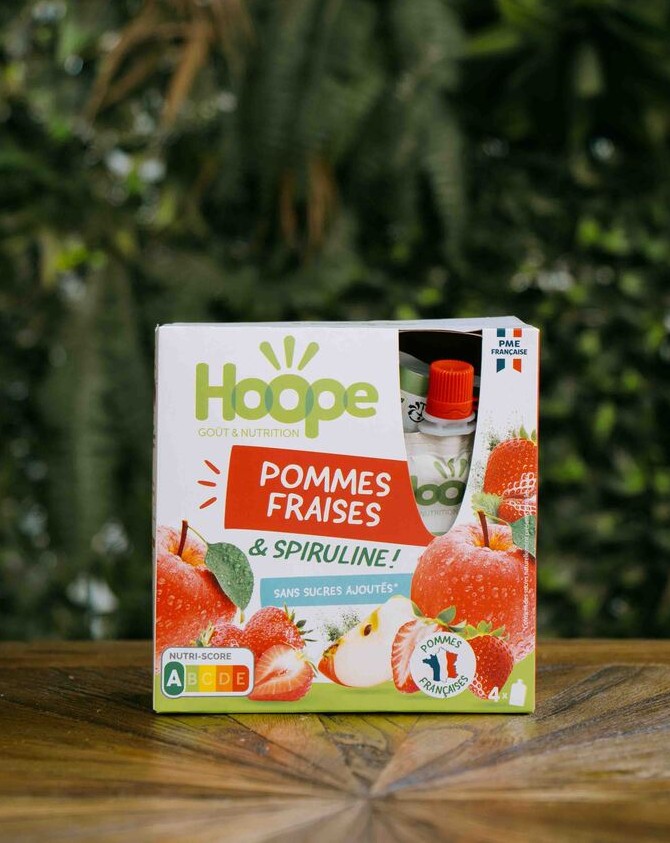 un paquet de compte pommes fraises posé sur une table en bois avec un fond de mur végétal