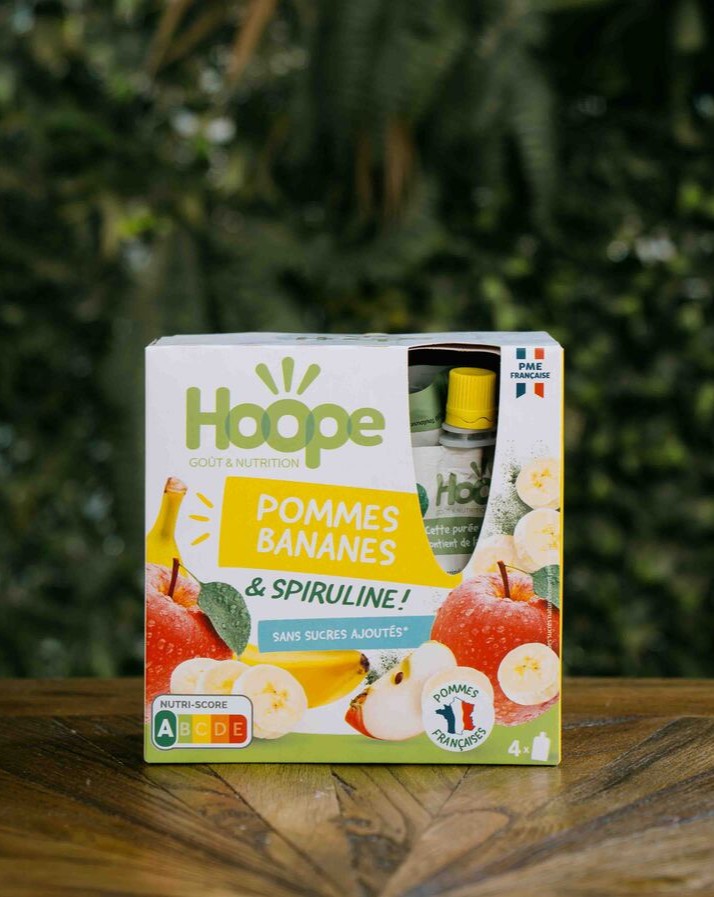un paquet de compotes pommes bananes posé sur une table en bois avec un fond de mur végétal