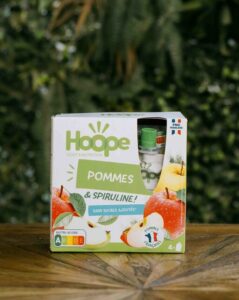 un paquet de compote pommes posé sur une table en bois avec un fond de mur végétal