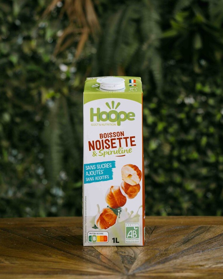une boisson végétale noisette posée sur une table en bois avec un fond de mur végétal