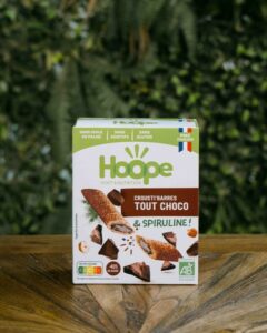 1 paquet de crousti barres tout choco posé sur une table en bois avec un fond de mur végétal