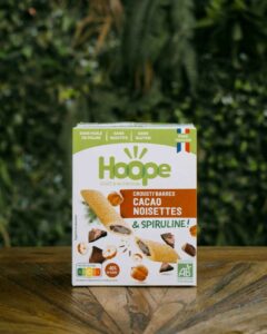 1 paquet de crousti barres cacao noisettes posé sur une table en bois avec un fond de mur végétal