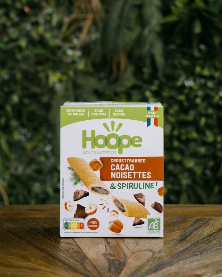 1 paquet de crousti barres cacao noisettes posé sur une table en bois avec un fond de mur végétal