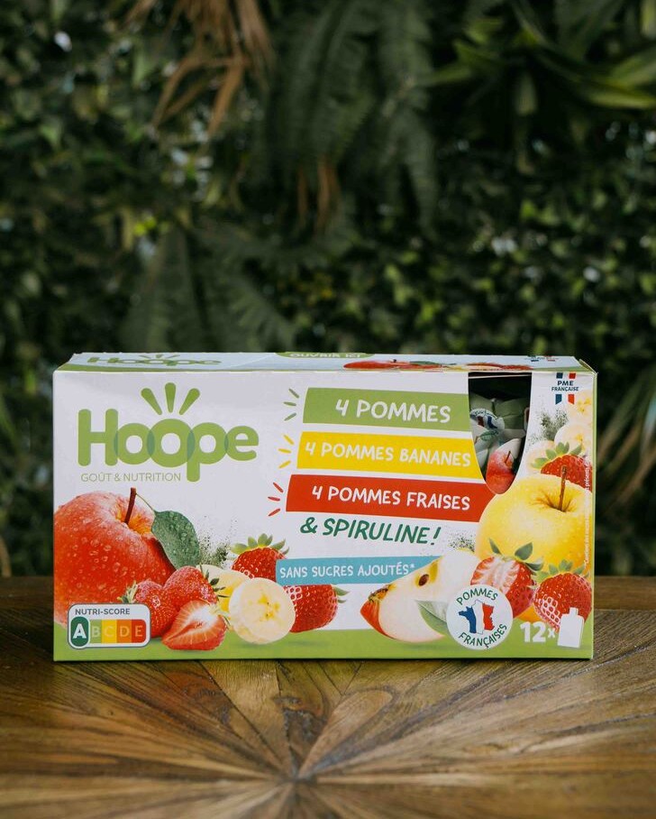 1 pack de 12 compotes pomme banane pomme fraise et pomme banane posé sur une table en bois avec un fond de mur végétal