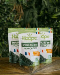 3 paquets de spiruline posés sur une table en bois avec un fond de mur végétal