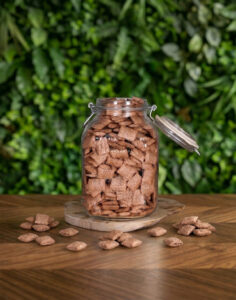 pot en verre avec des céréales fourrées chocolat posé sur une table en bois avec un fond végétal