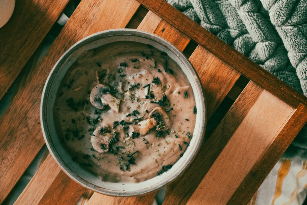 bol contenant un velouté de châtaignes avec des champignons parsemés et de la spiruline verte, sur un plateau en bois et un plaid vert
