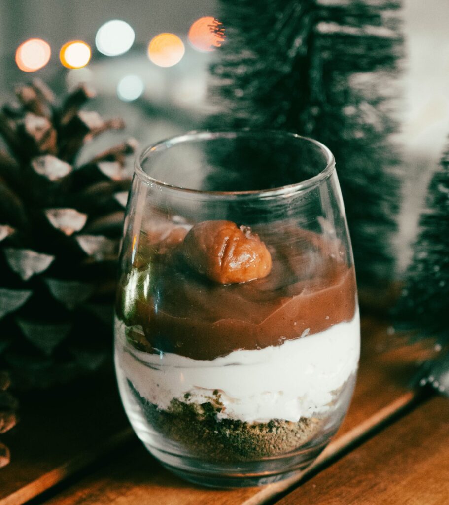 verrine composée de 3 couches : biscuit, mascarpone et crème de marron surmontée d'une chataigne, sur fond de pomme de pin, sapin et guirlande