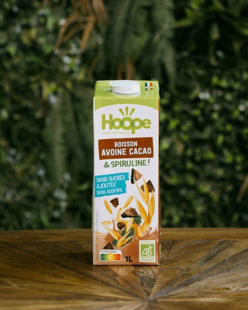 une bouteille de boisson avoine cacao posée sur une table en bois avec un fond de mur végétal